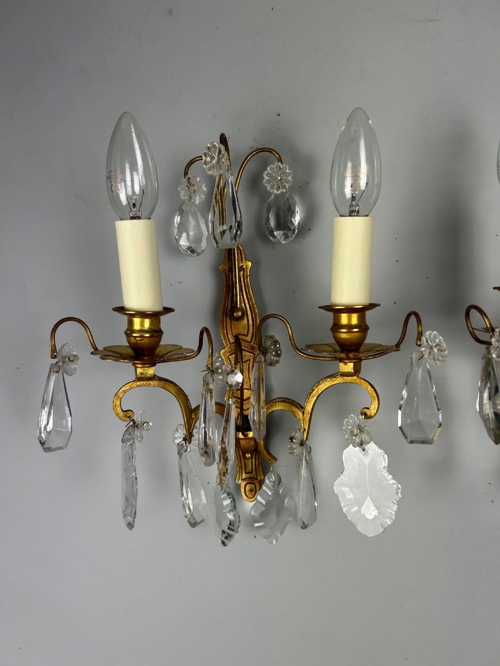 A pair of antique twin-arm wall lights featuring gilded frames and cascading crystal drops against a neutral background. View VI