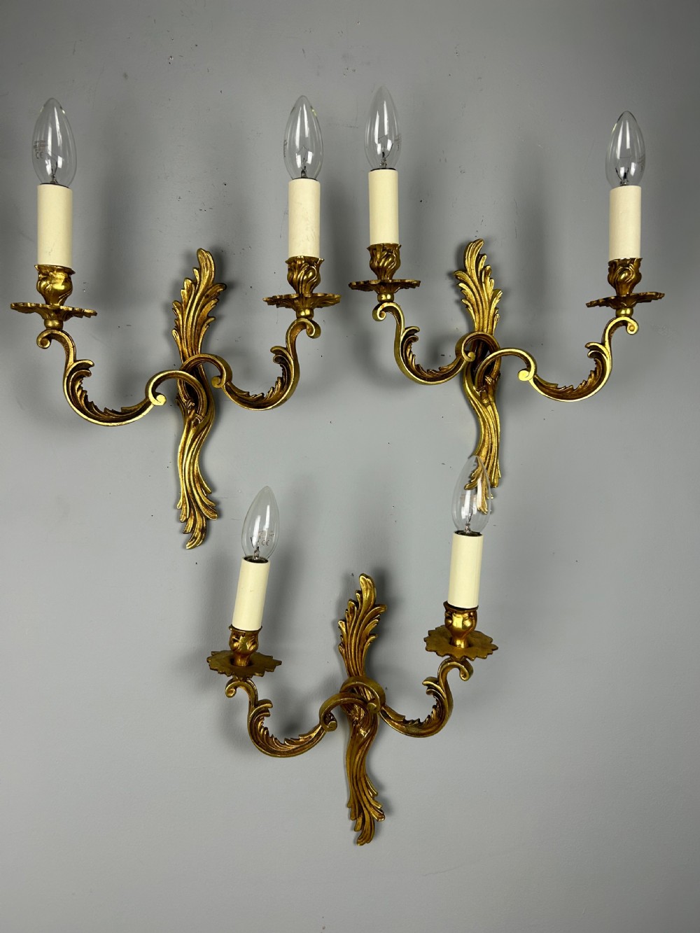 A set of three French gilt metal wall sconces featuring scrolled arms and decorative acanthus leaf backplates, fitted with candle-style bulbs. View II