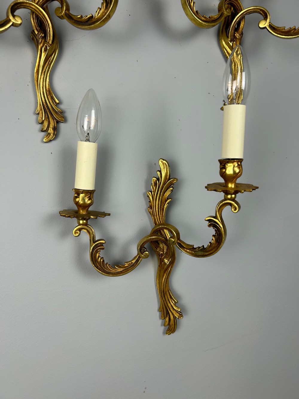 A set of three French gilt metal wall sconces featuring scrolled arms and decorative acanthus leaf backplates, fitted with candle-style bulbs. View III