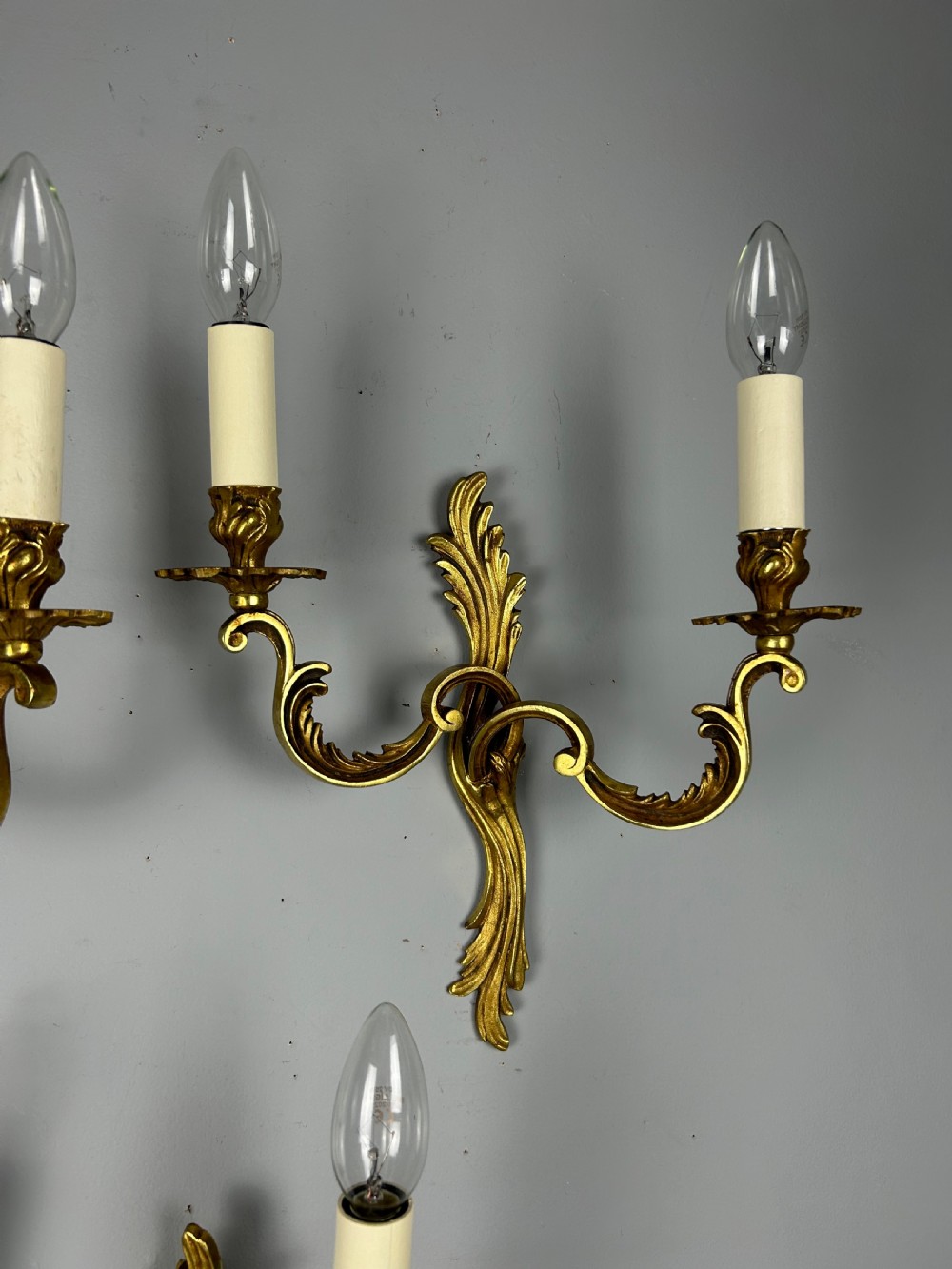 A set of three French gilt metal wall sconces featuring scrolled arms and decorative acanthus leaf backplates, fitted with candle-style bulbs. View IV