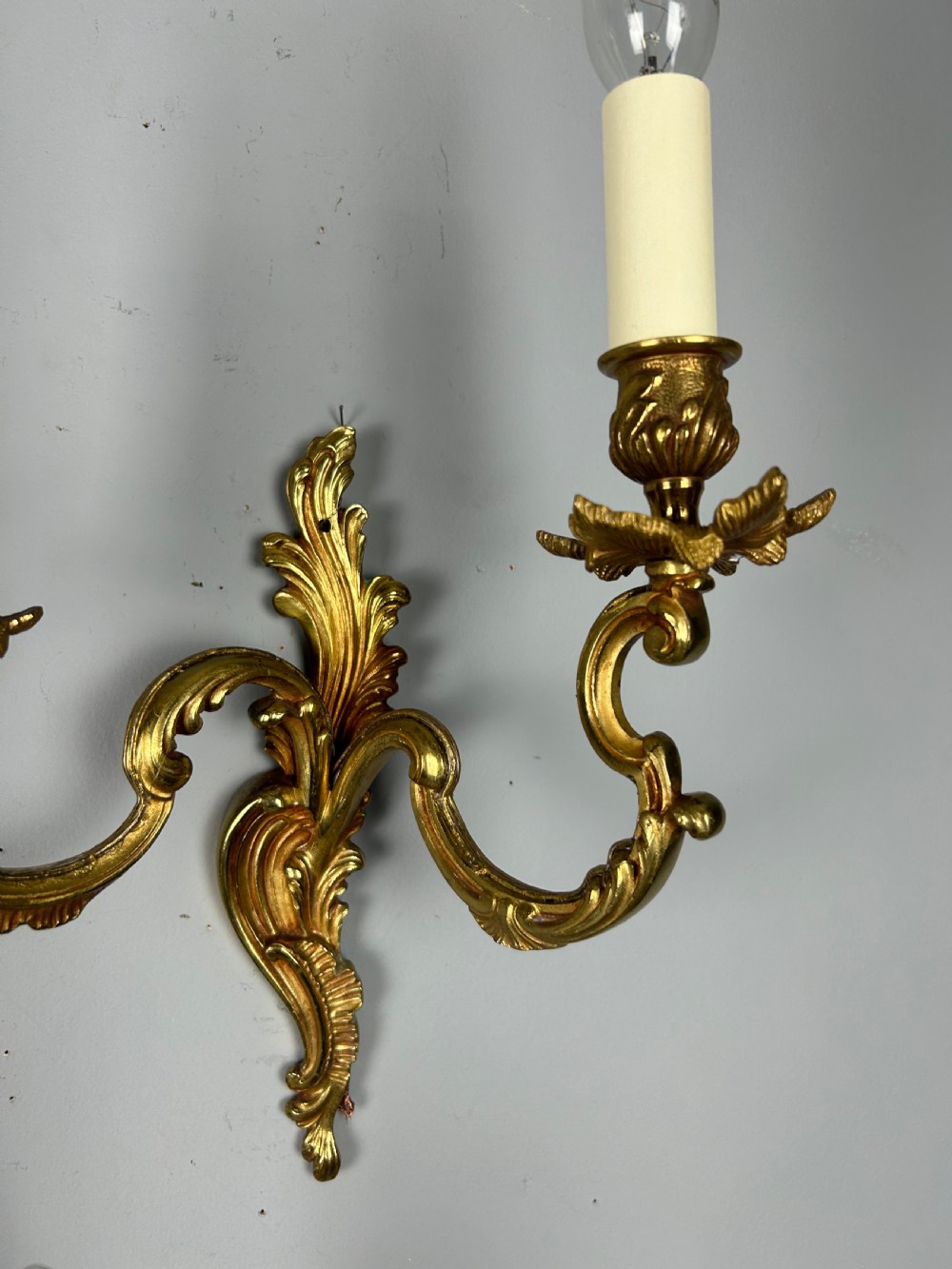 A set of three antique French gilded twin arm wall lights mounted against a neutral grey wall. View III