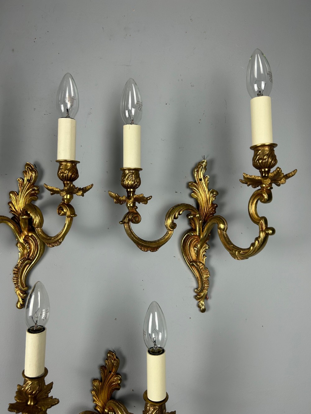 A set of three antique French gilded twin arm wall lights mounted against a neutral grey wall. View V