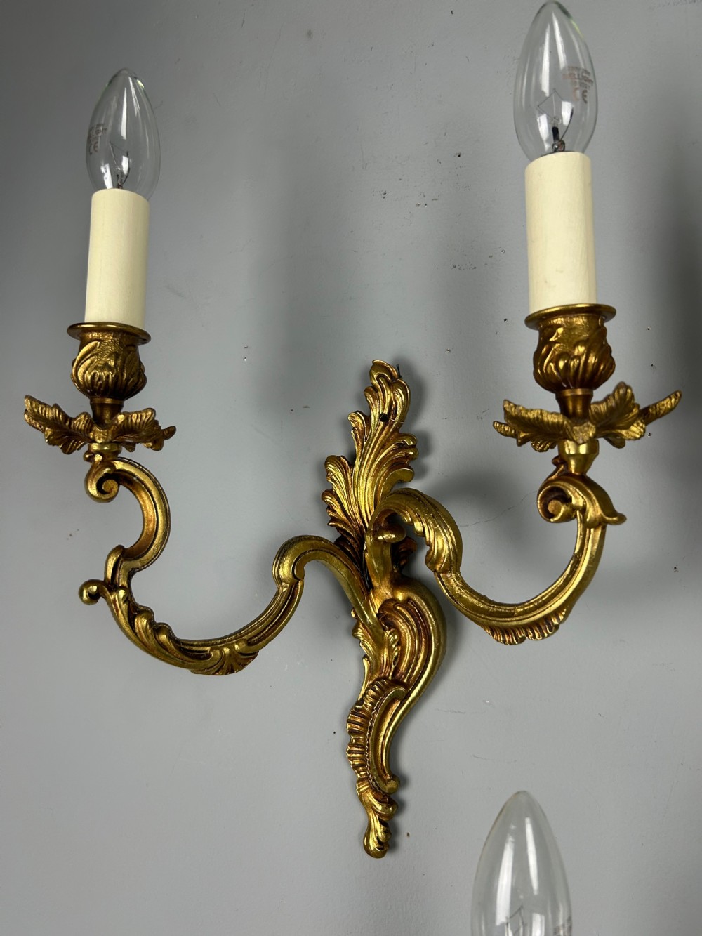 A set of three antique French gilded twin arm wall lights mounted against a neutral grey wall. View VI