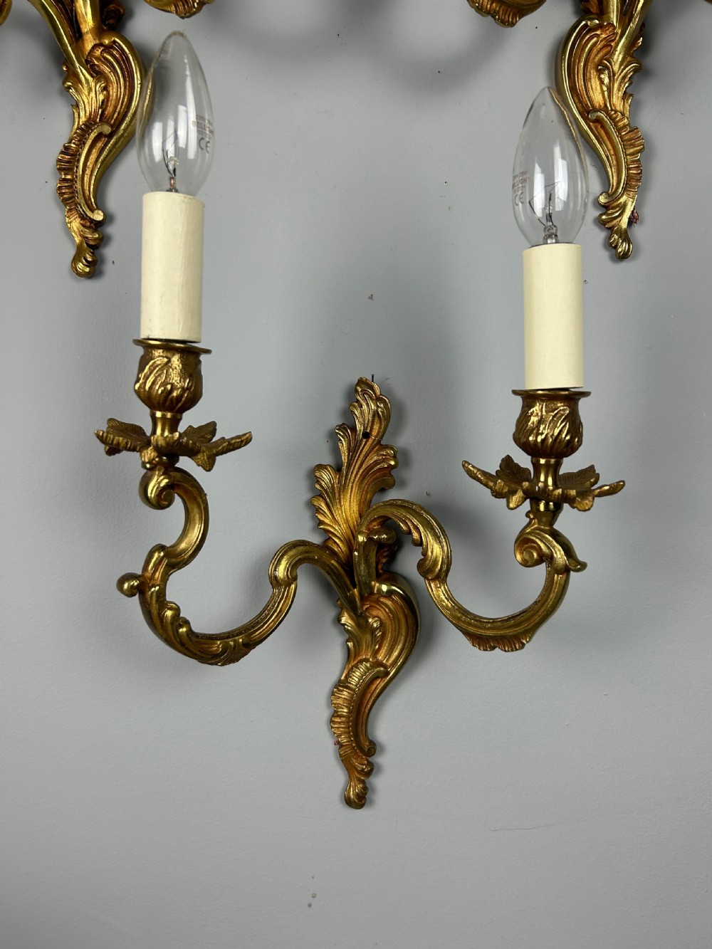A set of three antique French gilded twin arm wall lights mounted against a neutral grey wall. View VII