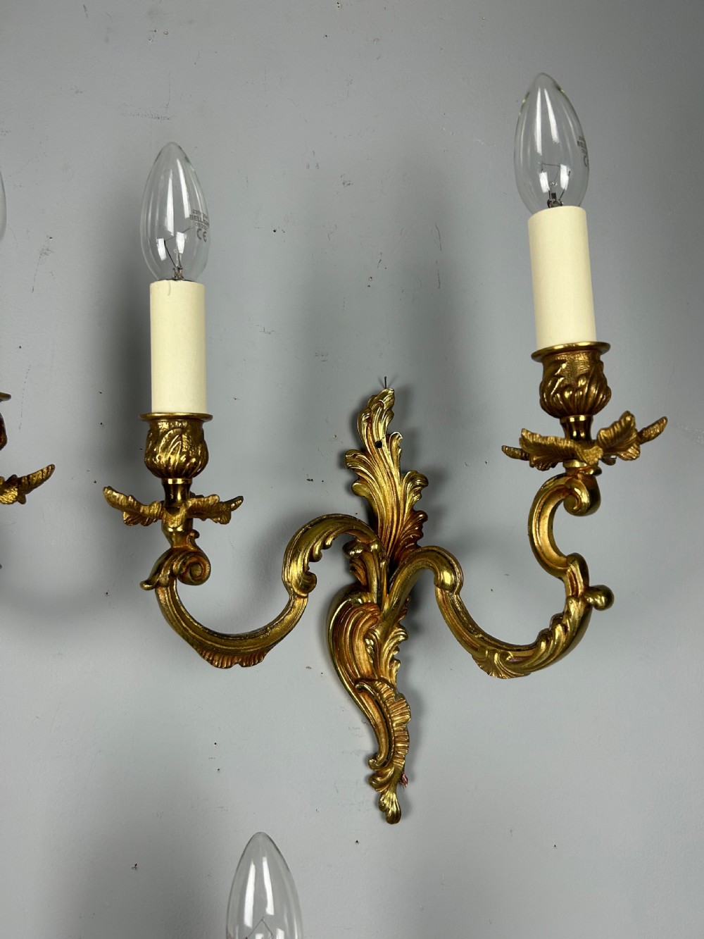 A set of three antique French gilded twin arm wall lights mounted against a neutral grey wall. View VIII