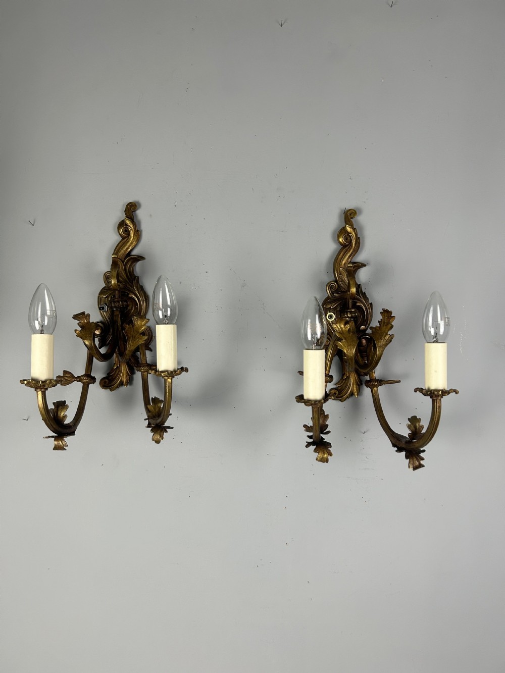 A pair of nineteenth-century French gilt bronze two-arm wall sconces featuring ornate acanthus leaf scrollwork and faux-candle sleeves.