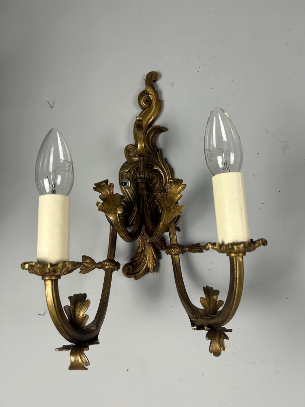 A pair of nineteenth-century French gilt bronze two-arm wall sconces featuring ornate acanthus leaf scrollwork and faux-candle sleeves. View III