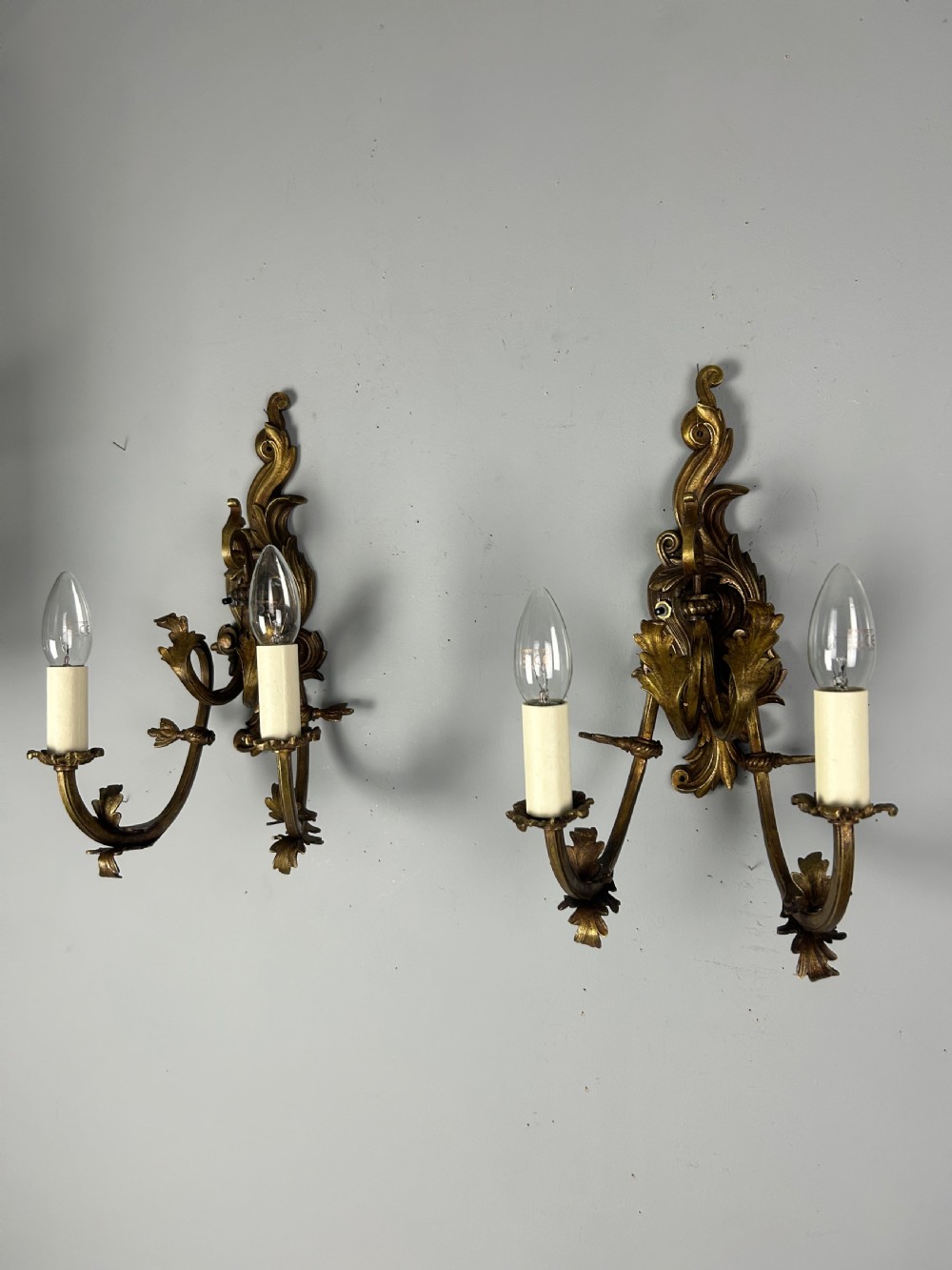 A pair of nineteenth-century French gilt bronze two-arm wall sconces featuring ornate acanthus leaf scrollwork and faux-candle sleeves. View V