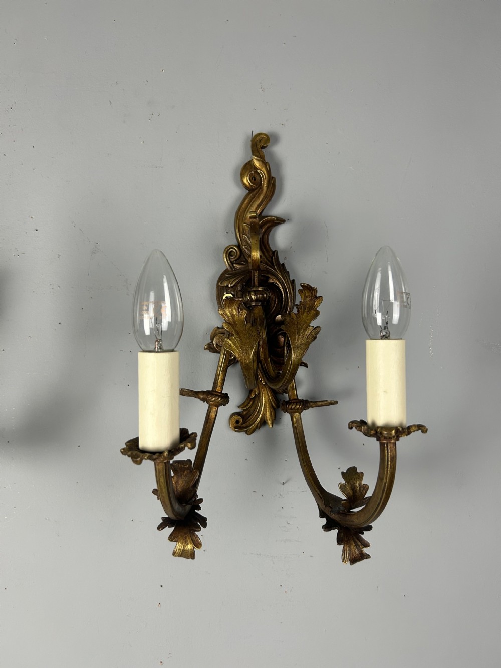 A pair of nineteenth-century French gilt bronze two-arm wall sconces featuring ornate acanthus leaf scrollwork and faux-candle sleeves. View VII