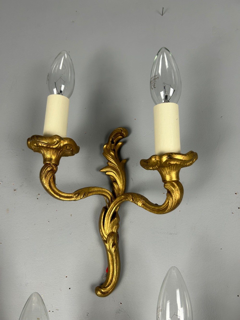 Set of three French gilt brass two-arm wall sconces featuring leaf ornamentation and simulated candle sockets. View II