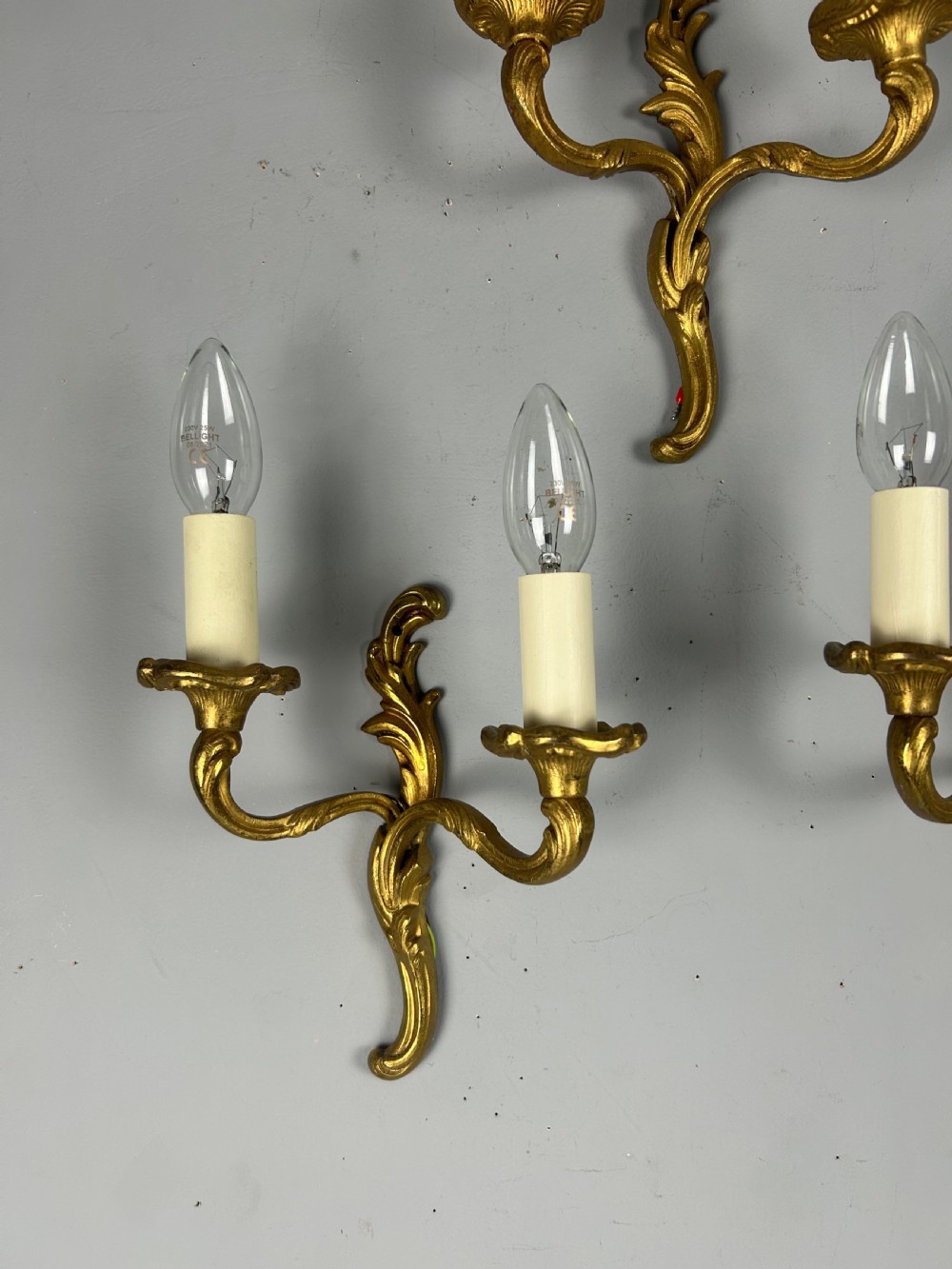 Set of three French gilt brass two-arm wall sconces featuring leaf ornamentation and simulated candle sockets. View III