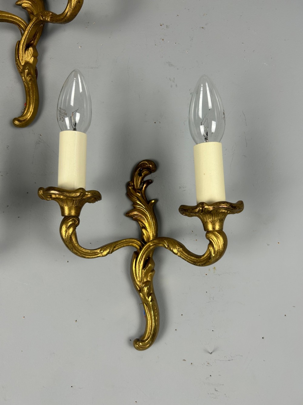 Set of three French gilt brass two-arm wall sconces featuring leaf ornamentation and simulated candle sockets. View IV