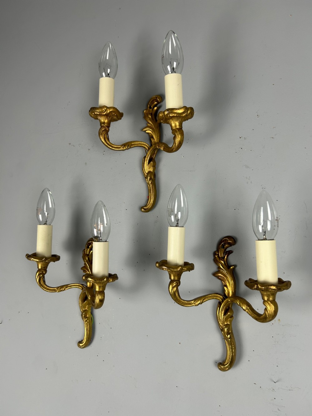 Set of three French gilt brass two-arm wall sconces featuring leaf ornamentation and simulated candle sockets. View V