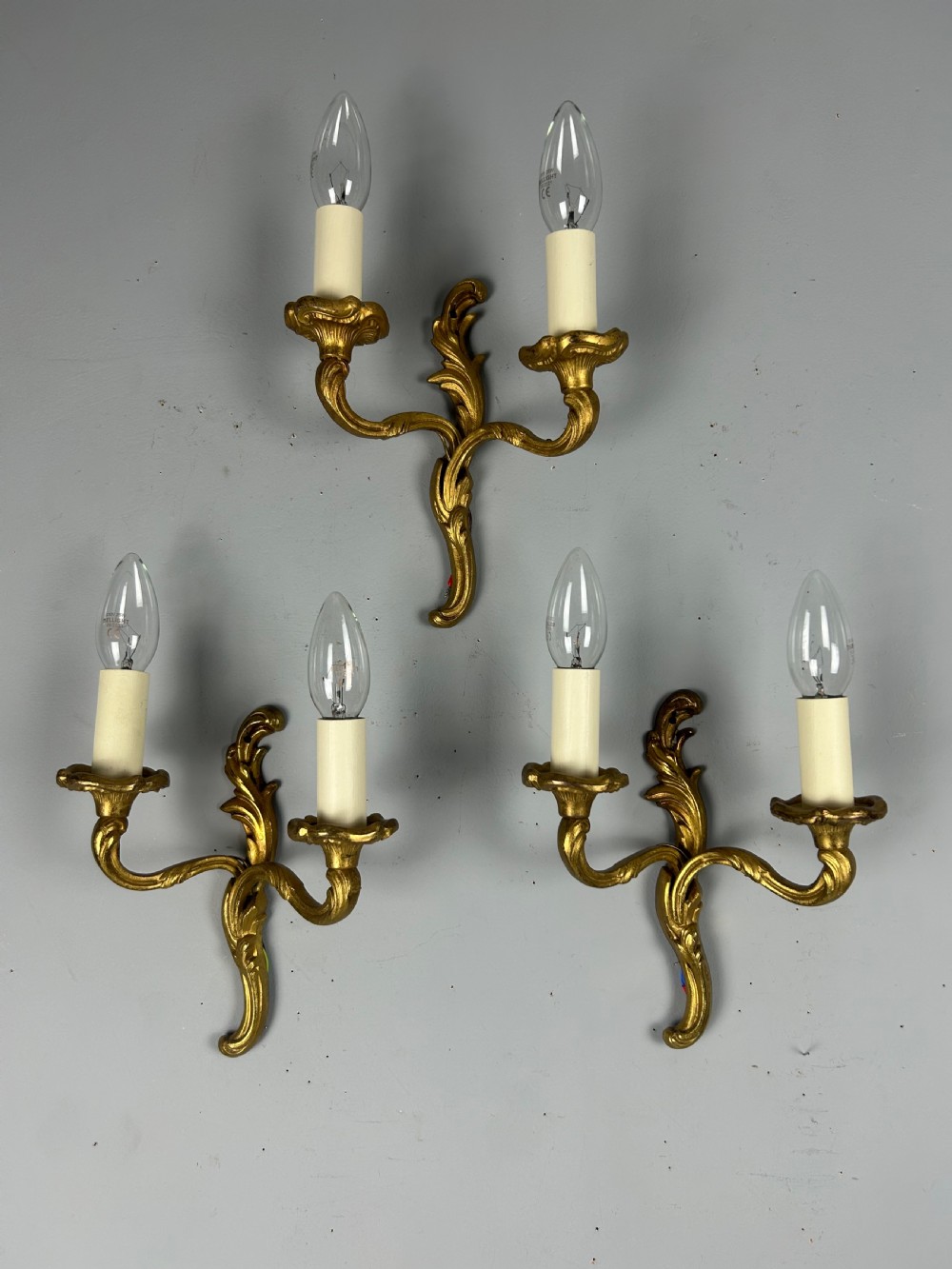 Set of three French gilt brass two-arm wall sconces featuring leaf ornamentation and simulated candle sockets. View VI