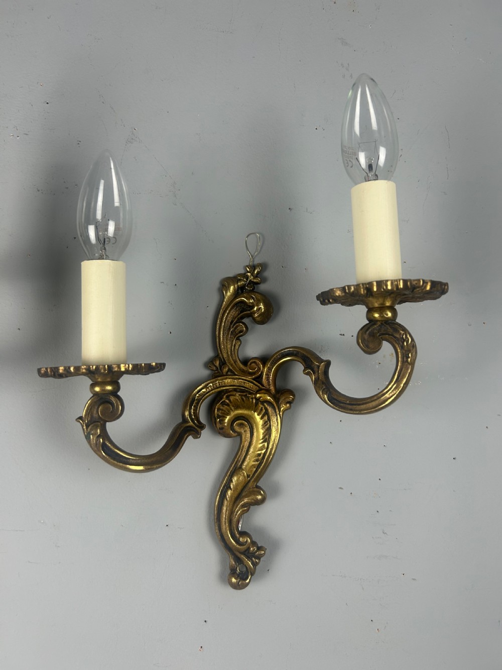 A pair of French Rococo style gilded brass twin-arm wall lights with foliate scrollwork and white candle sleeves. View VI