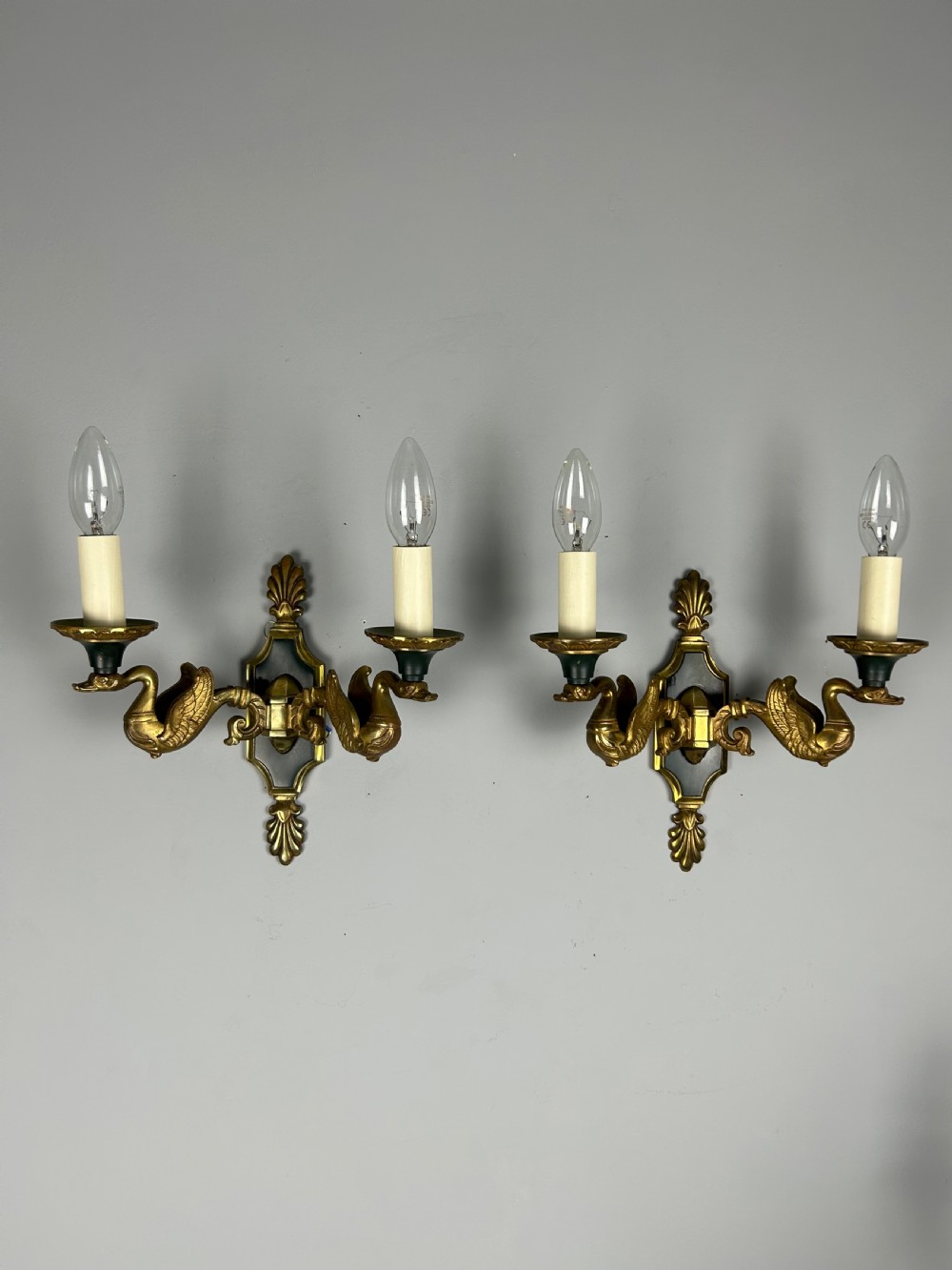 A pair of French Empire style double-arm gilt brass wall sconces featuring sculpted swan-neck branches and central palmette backplates.