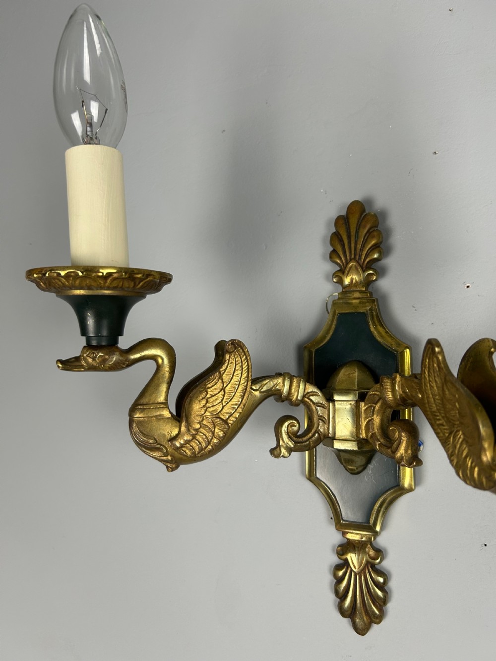 A pair of French Empire style double-arm gilt brass wall sconces featuring sculpted swan-neck branches and central palmette backplates. View V