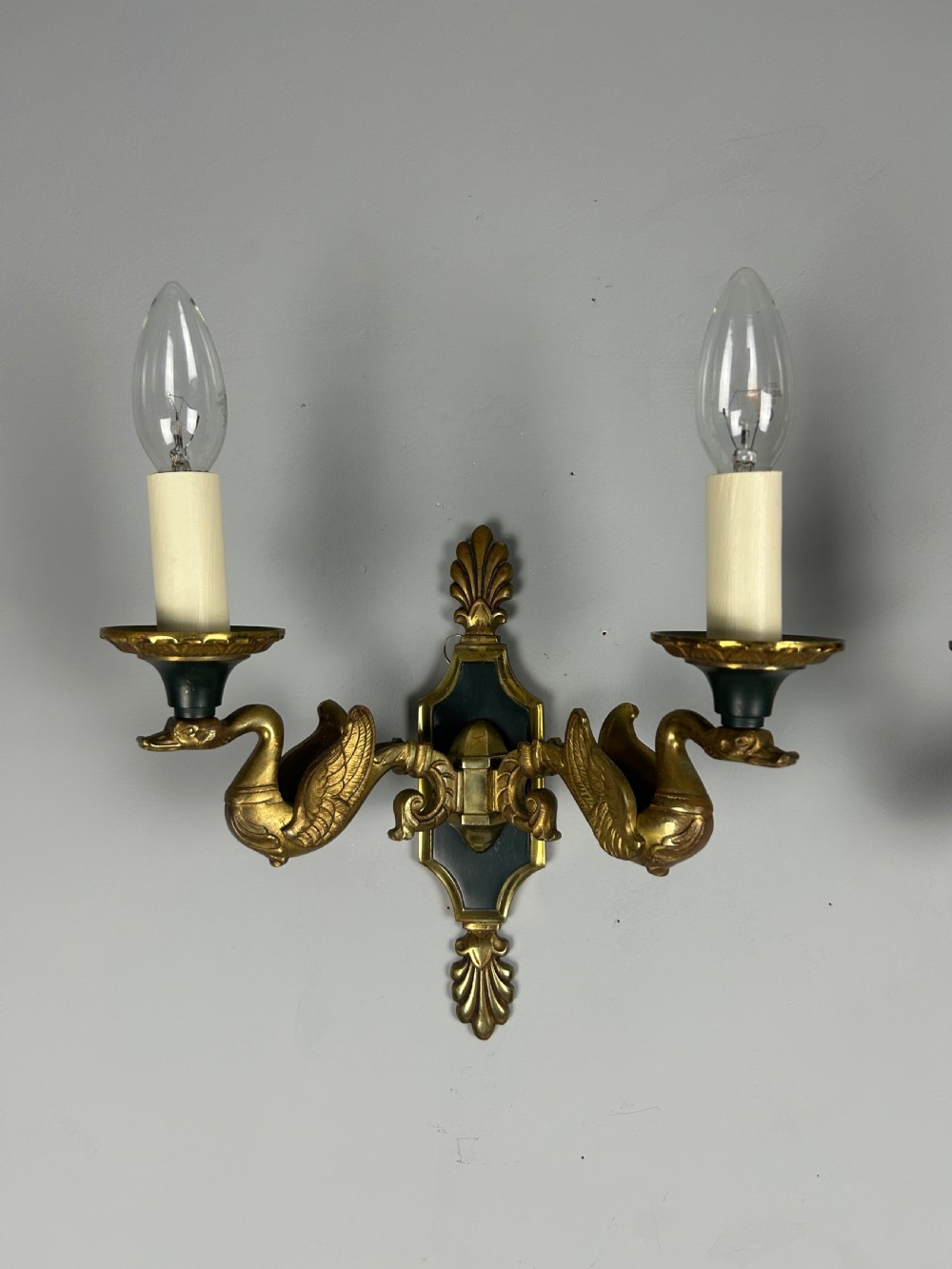 A pair of French Empire style double-arm gilt brass wall sconces featuring sculpted swan-neck branches and central palmette backplates. View X