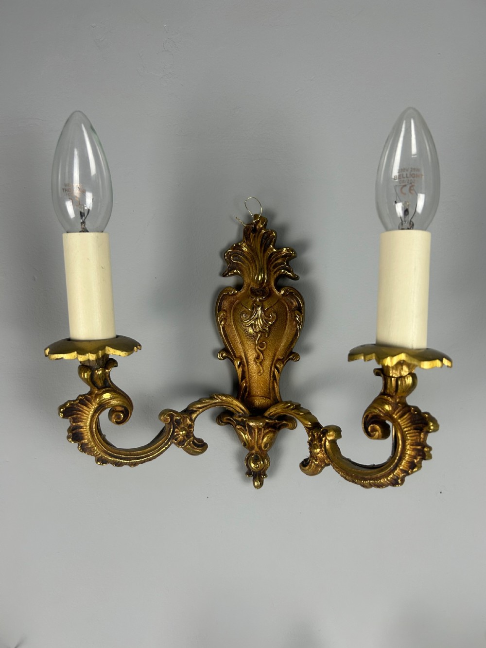 A set of three French Rococo style gilded brass wall lights with twin scroll arms and candle-shaped bulb holders. View II