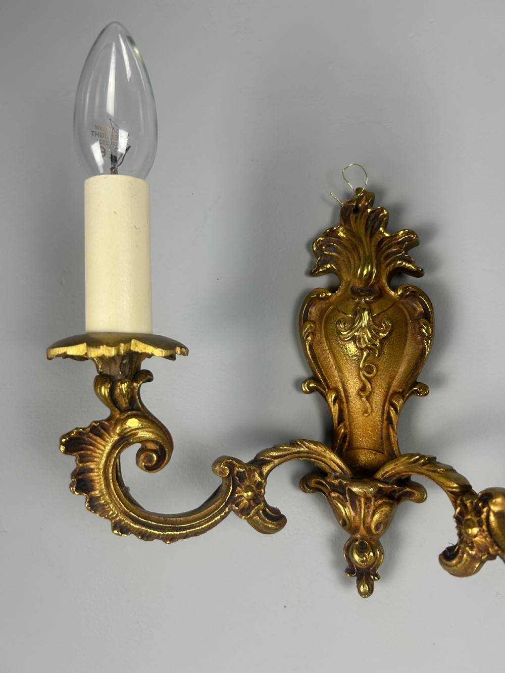 A set of three French Rococo style gilded brass wall lights with twin scroll arms and candle-shaped bulb holders. View III