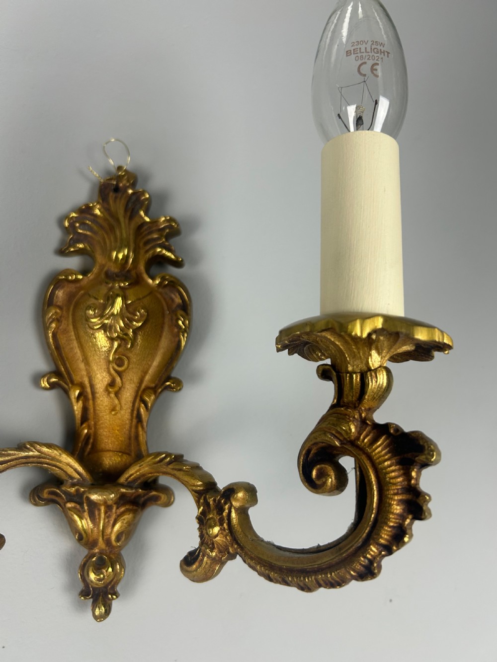 A set of three French Rococo style gilded brass wall lights with twin scroll arms and candle-shaped bulb holders. View IV