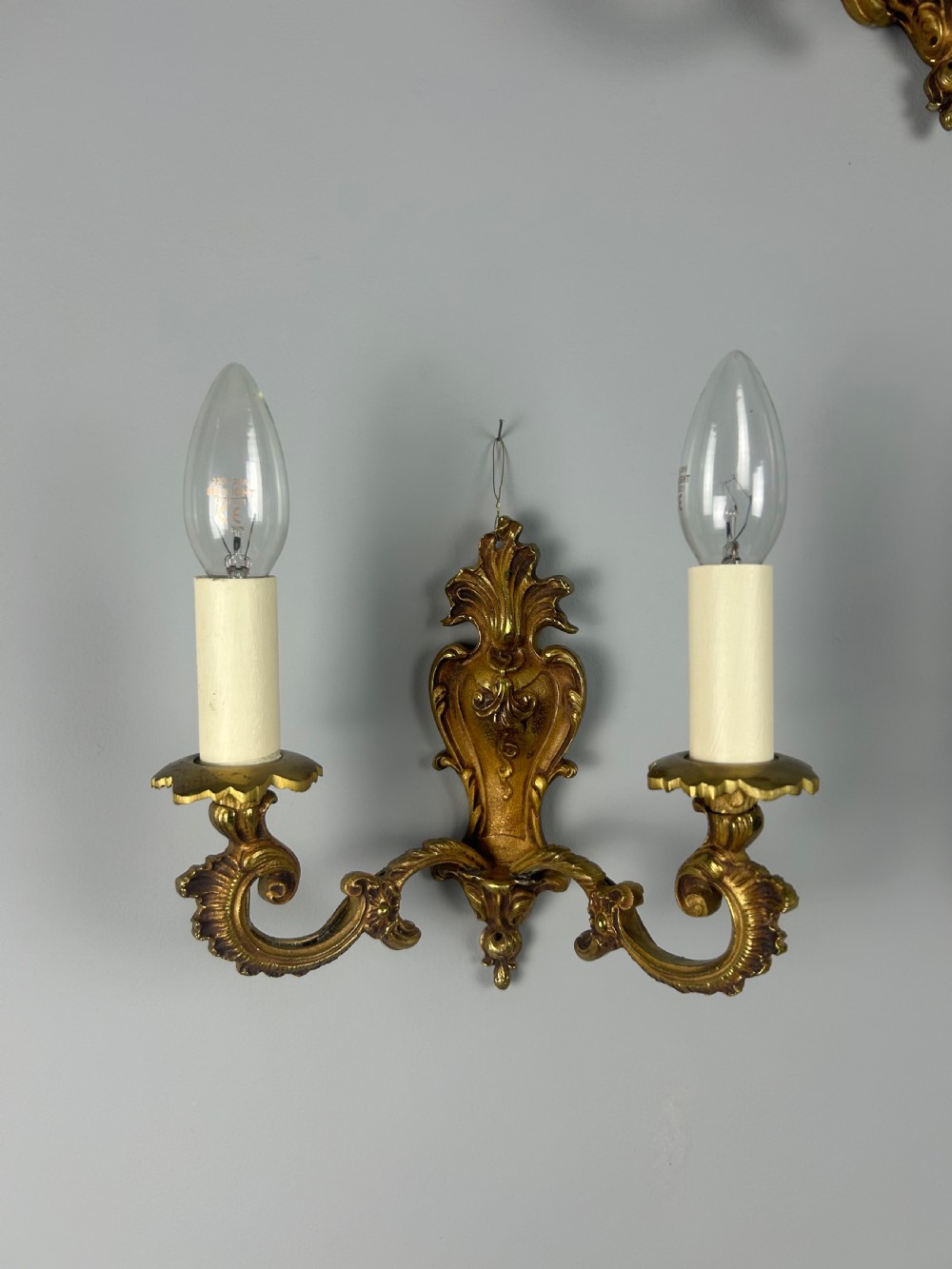 A set of three French Rococo style gilded brass wall lights with twin scroll arms and candle-shaped bulb holders. View VI
