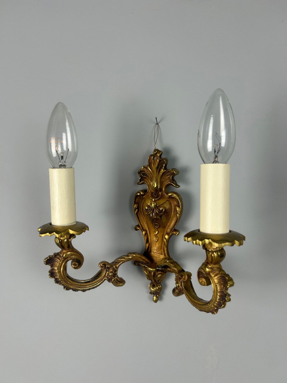 A set of three French Rococo style gilded brass wall lights with twin scroll arms and candle-shaped bulb holders. View VII