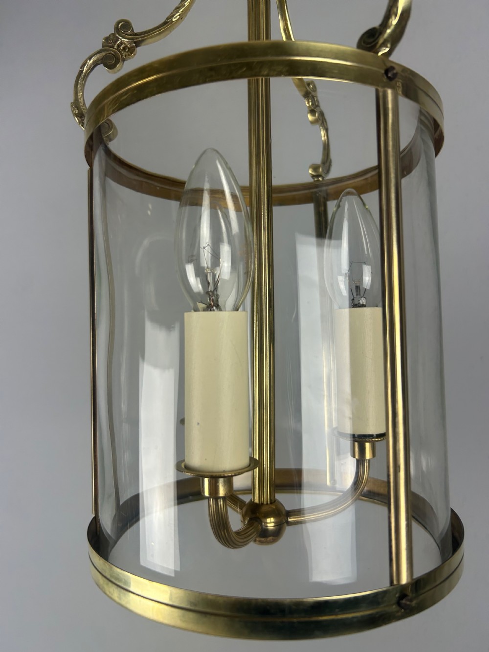A polished brass cylindrical pendant lantern with clear curved glass panels housing a three-light candle cluster inside. View VIII