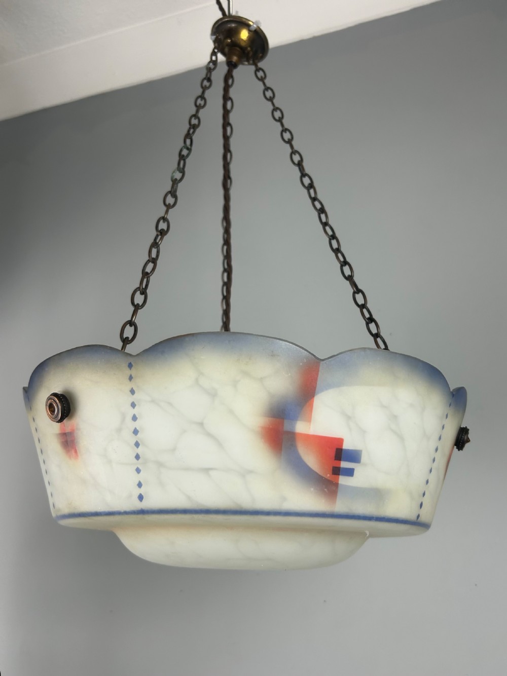An Art Deco frosted glass plafonnier ceiling light shade with painted blue and orange geometric patterns suspended by brass chains.