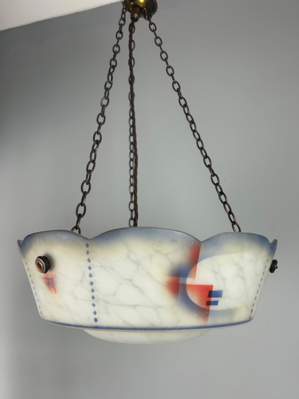 An Art Deco frosted glass plafonnier ceiling light shade with painted blue and orange geometric patterns suspended by brass chains. View II