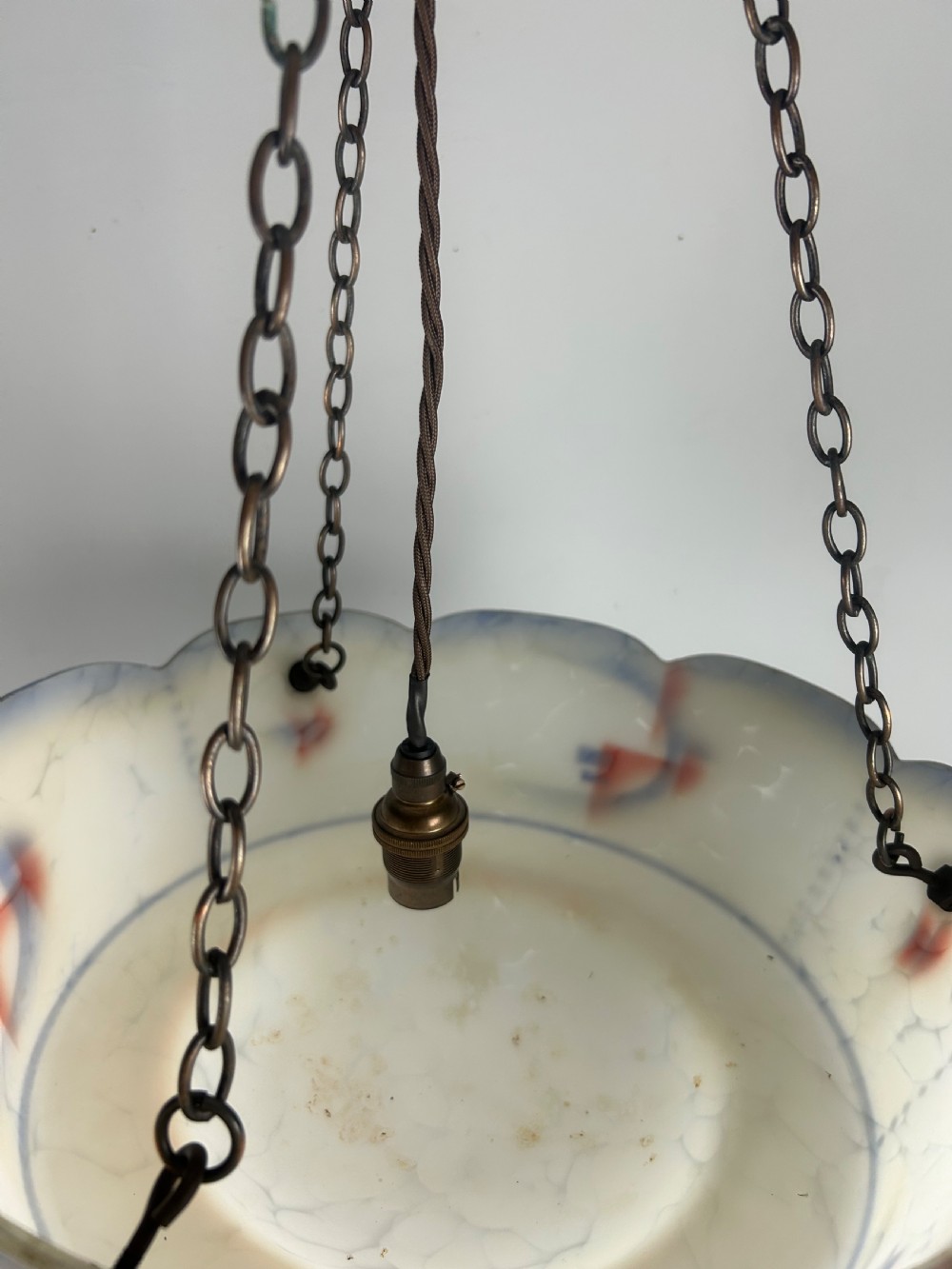 An Art Deco frosted glass plafonnier ceiling light shade with painted blue and orange geometric patterns suspended by brass chains. View IV