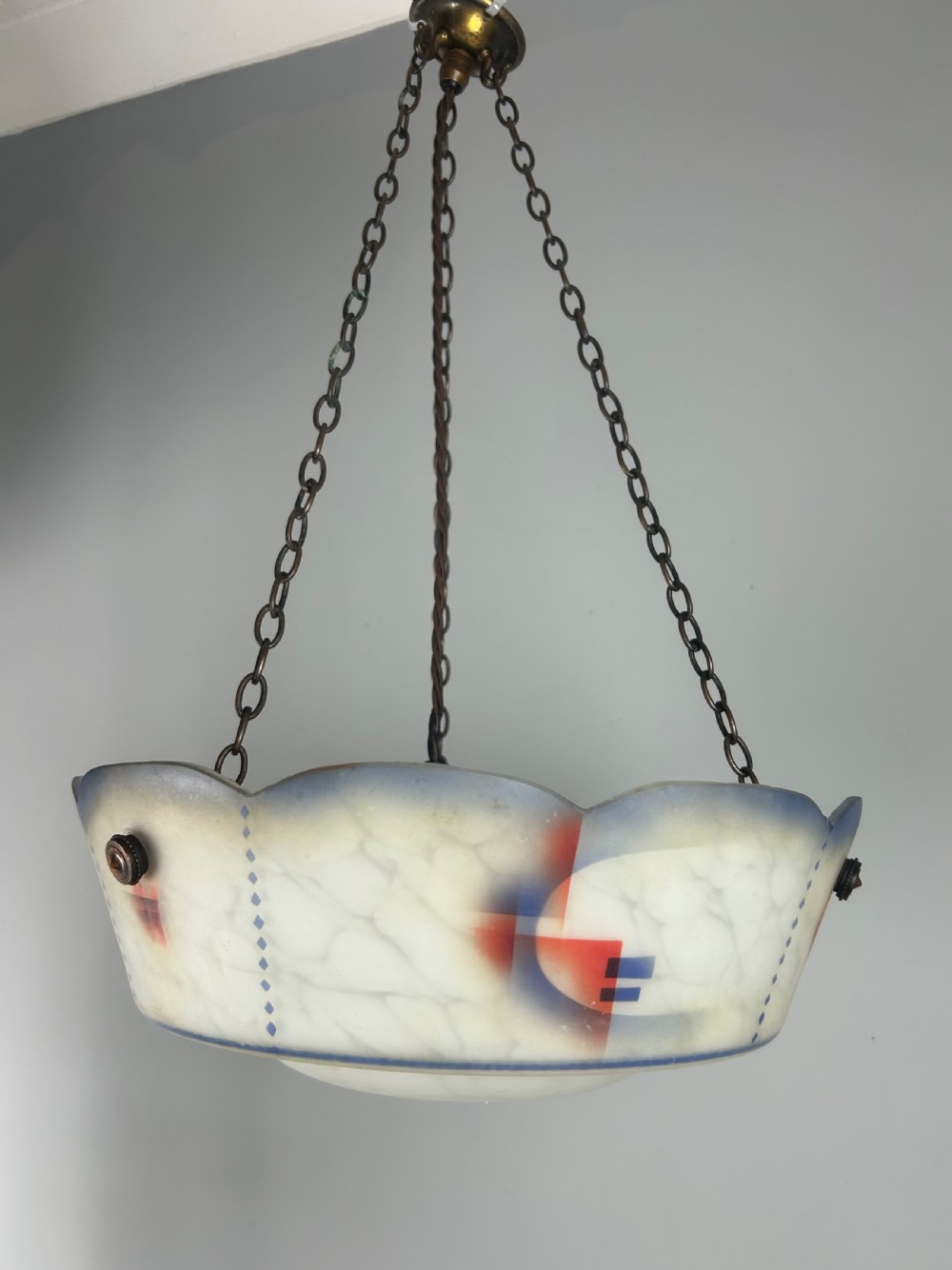An Art Deco frosted glass plafonnier ceiling light shade with painted blue and orange geometric patterns suspended by brass chains. View V