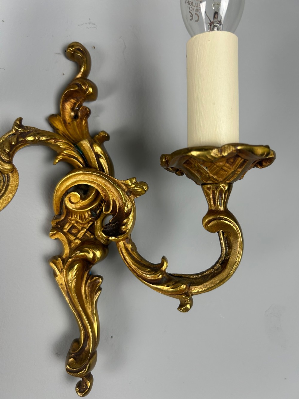 A pair of French Rococo style gilded bronze two-light wall sconces featuring acanthus leaf scrolls and candle-effect sleeves. View II