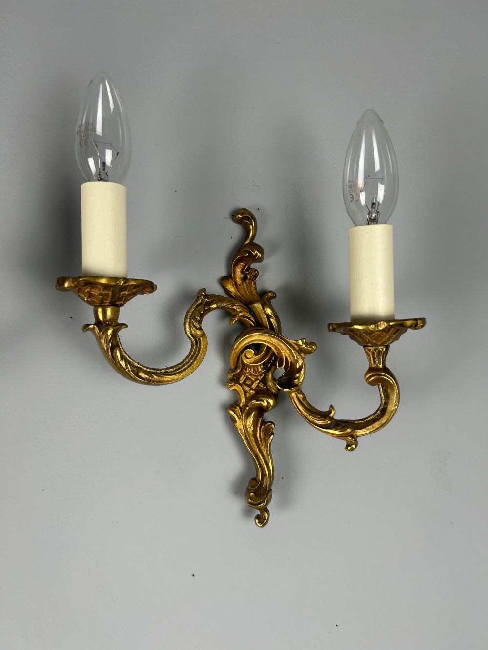 A pair of French Rococo style gilded bronze two-light wall sconces featuring acanthus leaf scrolls and candle-effect sleeves. View III