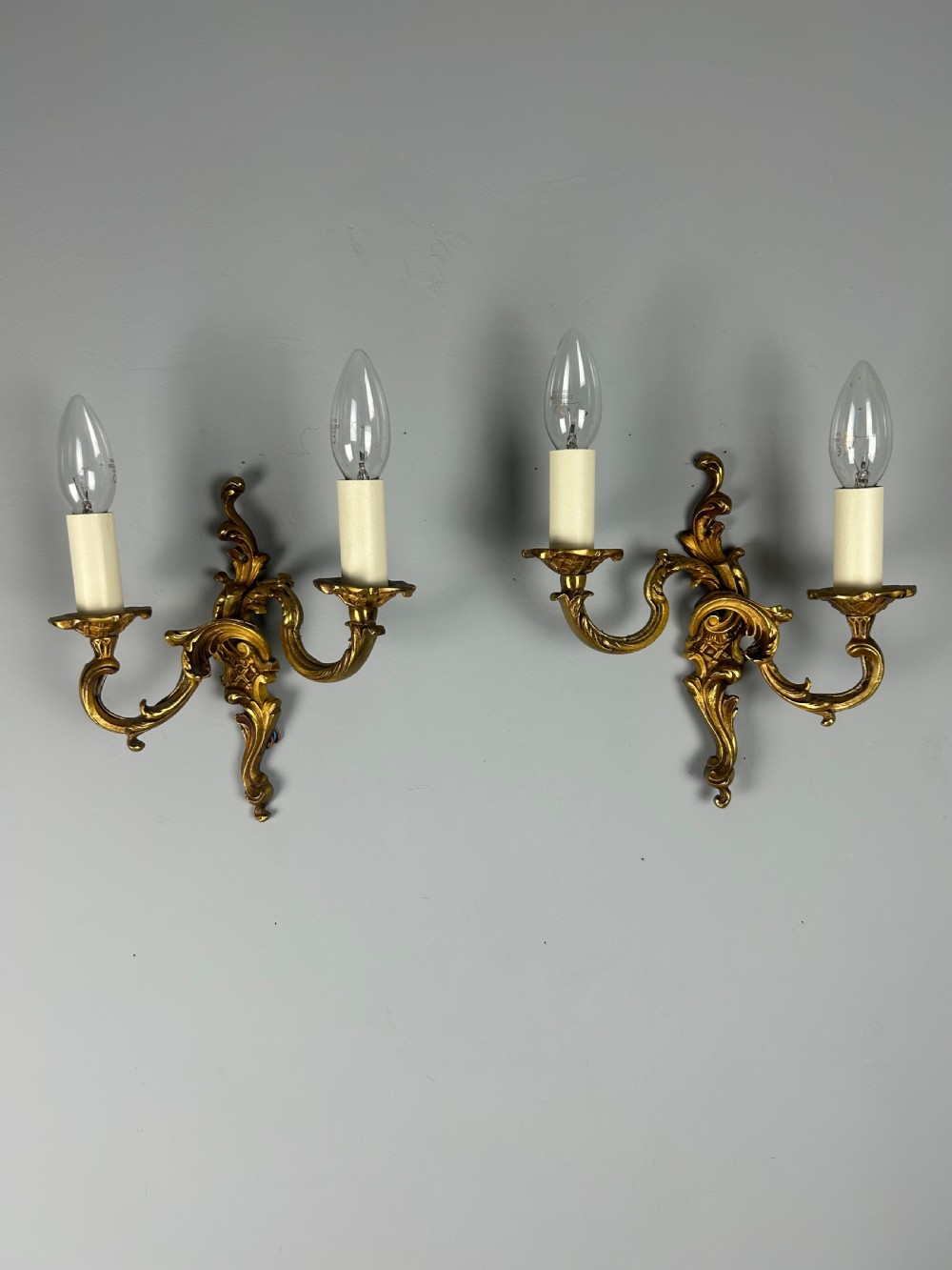 A pair of French Rococo style gilded bronze two-light wall sconces featuring acanthus leaf scrolls and candle-effect sleeves. View IV