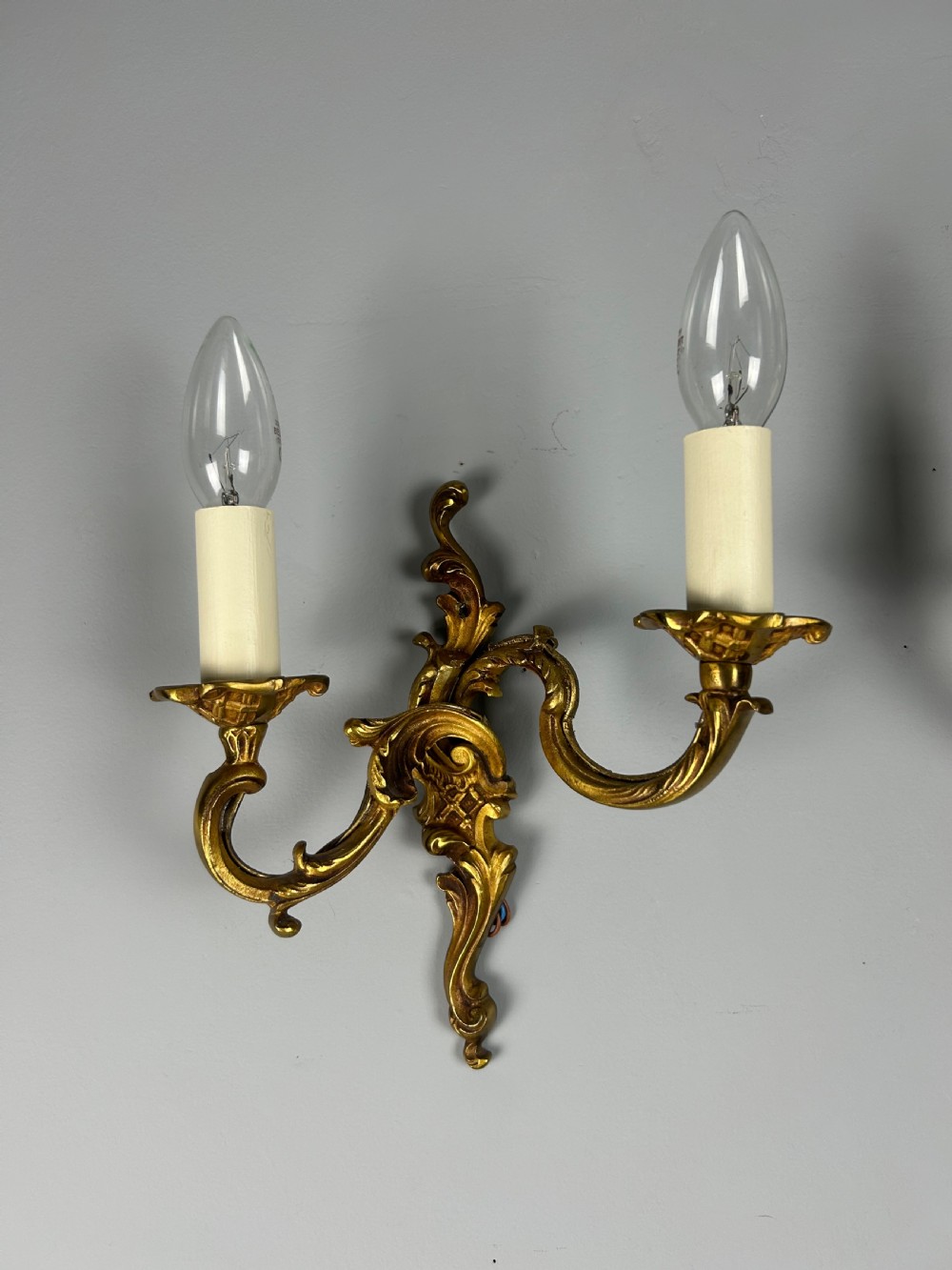 A pair of French Rococo style gilded bronze two-light wall sconces featuring acanthus leaf scrolls and candle-effect sleeves. View V