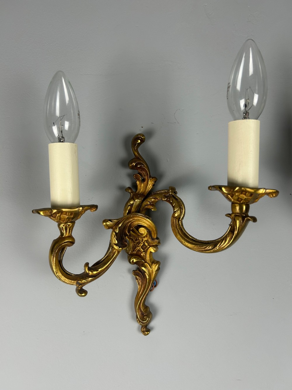 A pair of French Rococo style gilded bronze two-light wall sconces featuring acanthus leaf scrolls and candle-effect sleeves. View IX