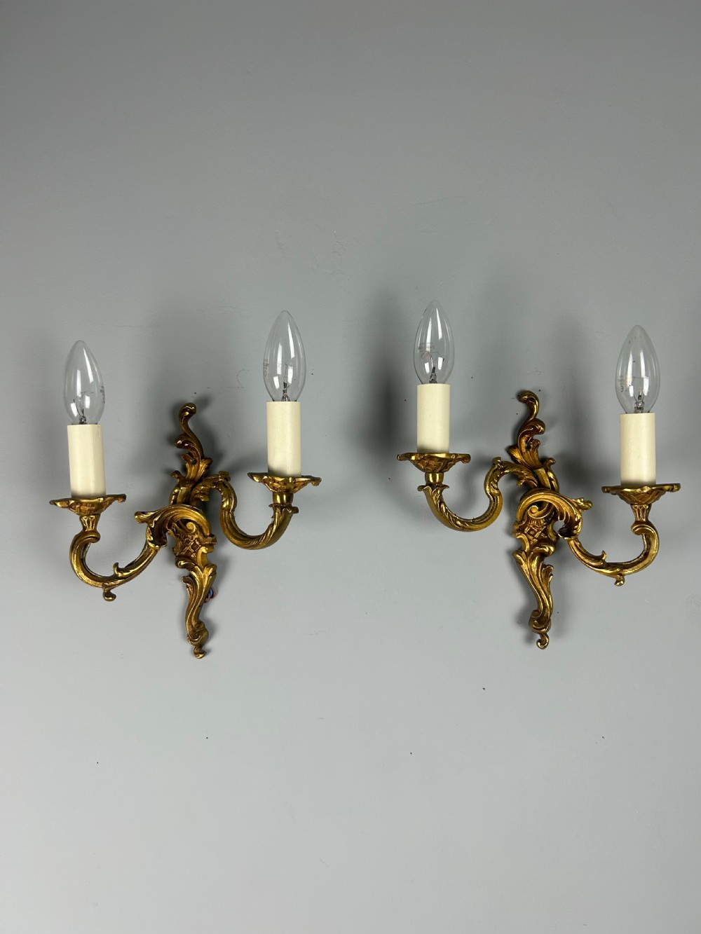 A pair of French Rococo style gilded bronze two-light wall sconces featuring acanthus leaf scrolls and candle-effect sleeves. View X