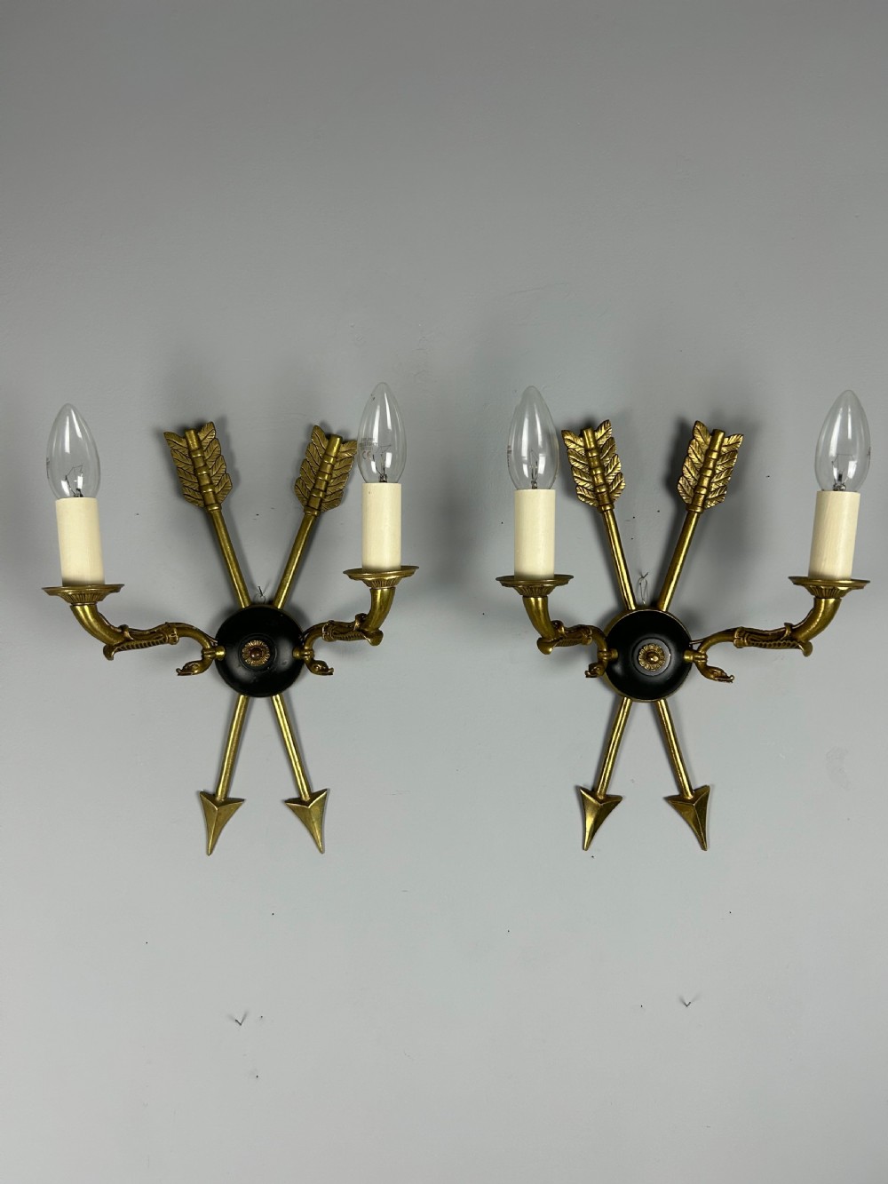 A pair of French Empire style brass and black metal wall sconces featuring crossed arrow backplates and swan neck candle arms.