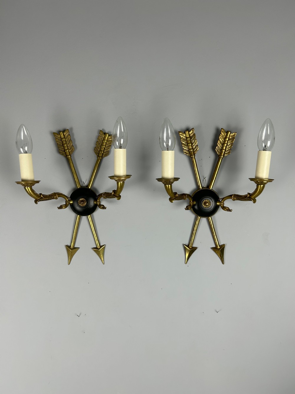 A pair of French Empire style brass and black metal wall sconces featuring crossed arrow backplates and swan neck candle arms. View II
