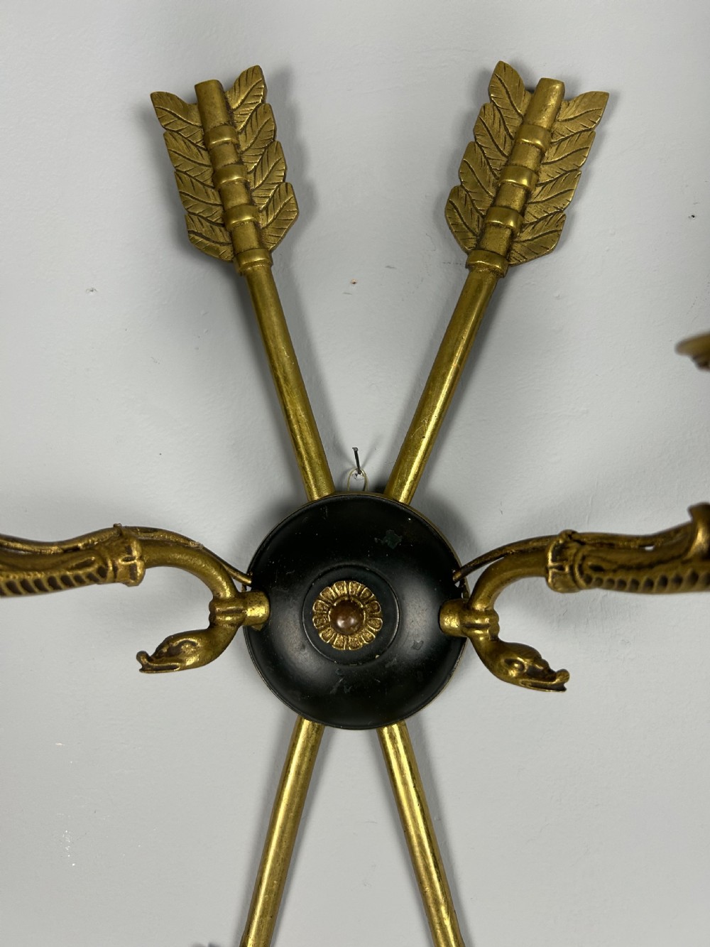 A pair of French Empire style brass and black metal wall sconces featuring crossed arrow backplates and swan neck candle arms. View V