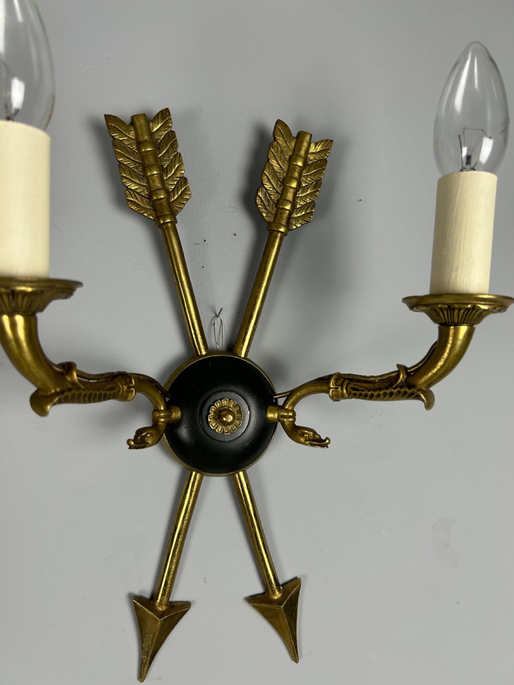 A pair of French Empire style brass and black metal wall sconces featuring crossed arrow backplates and swan neck candle arms. View VII