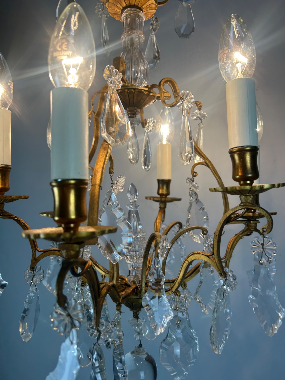 A French brass six-light chandelier featuring curved scroll arms, candle sleeves, and suspended faceted crystal glass droplets. View III