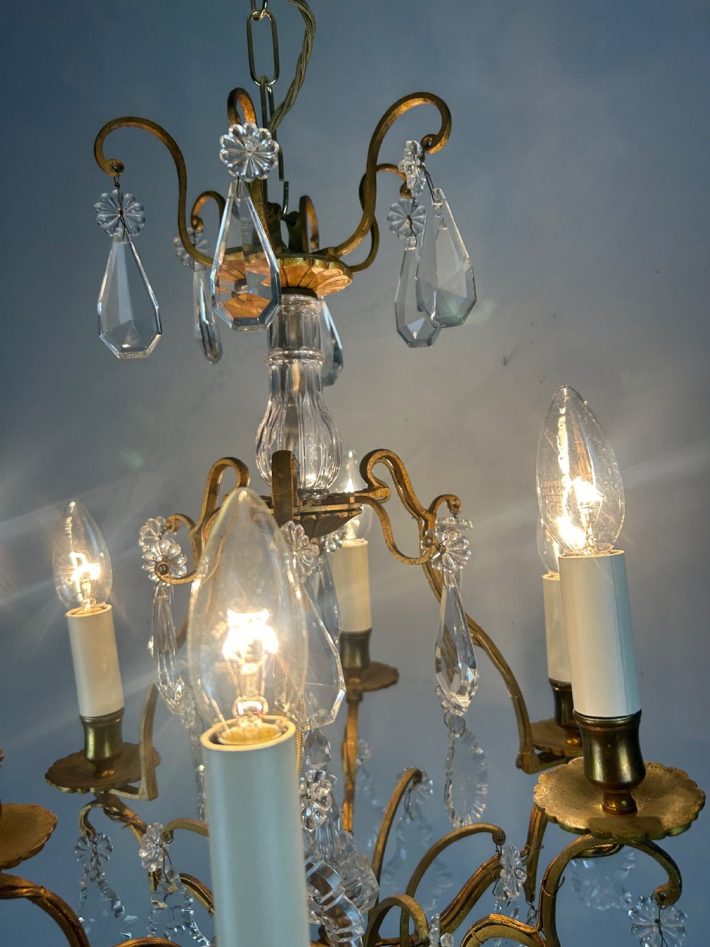 A French brass six-light chandelier featuring curved scroll arms, candle sleeves, and suspended faceted crystal glass droplets. View IV