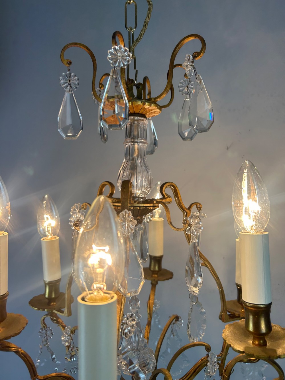 A French brass six-light chandelier featuring curved scroll arms, candle sleeves, and suspended faceted crystal glass droplets. View V