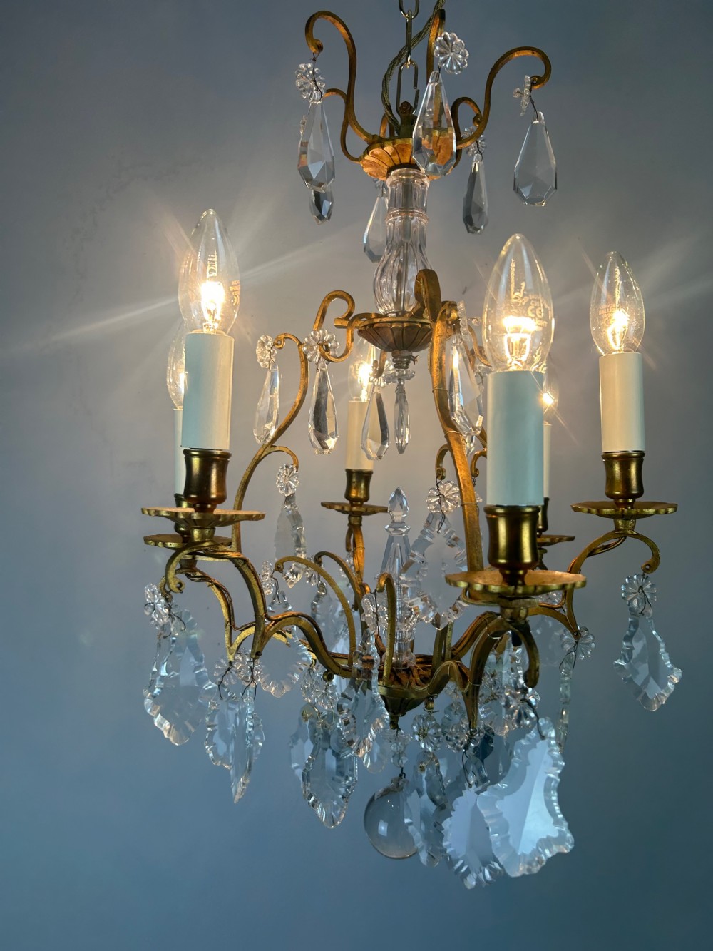 A French brass six-light chandelier featuring curved scroll arms, candle sleeves, and suspended faceted crystal glass droplets. View VI