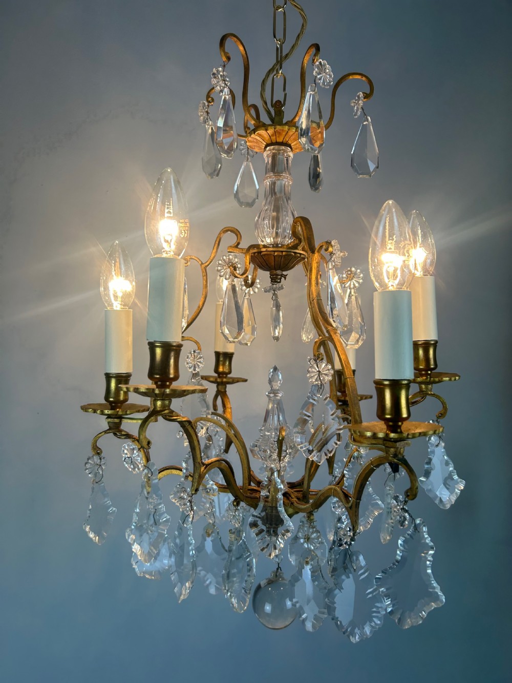 A French brass six-light chandelier featuring curved scroll arms, candle sleeves, and suspended faceted crystal glass droplets. View VII