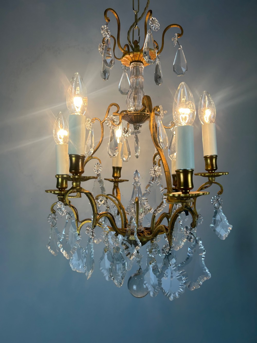A French brass six-light chandelier featuring curved scroll arms, candle sleeves, and suspended faceted crystal glass droplets. View VIII