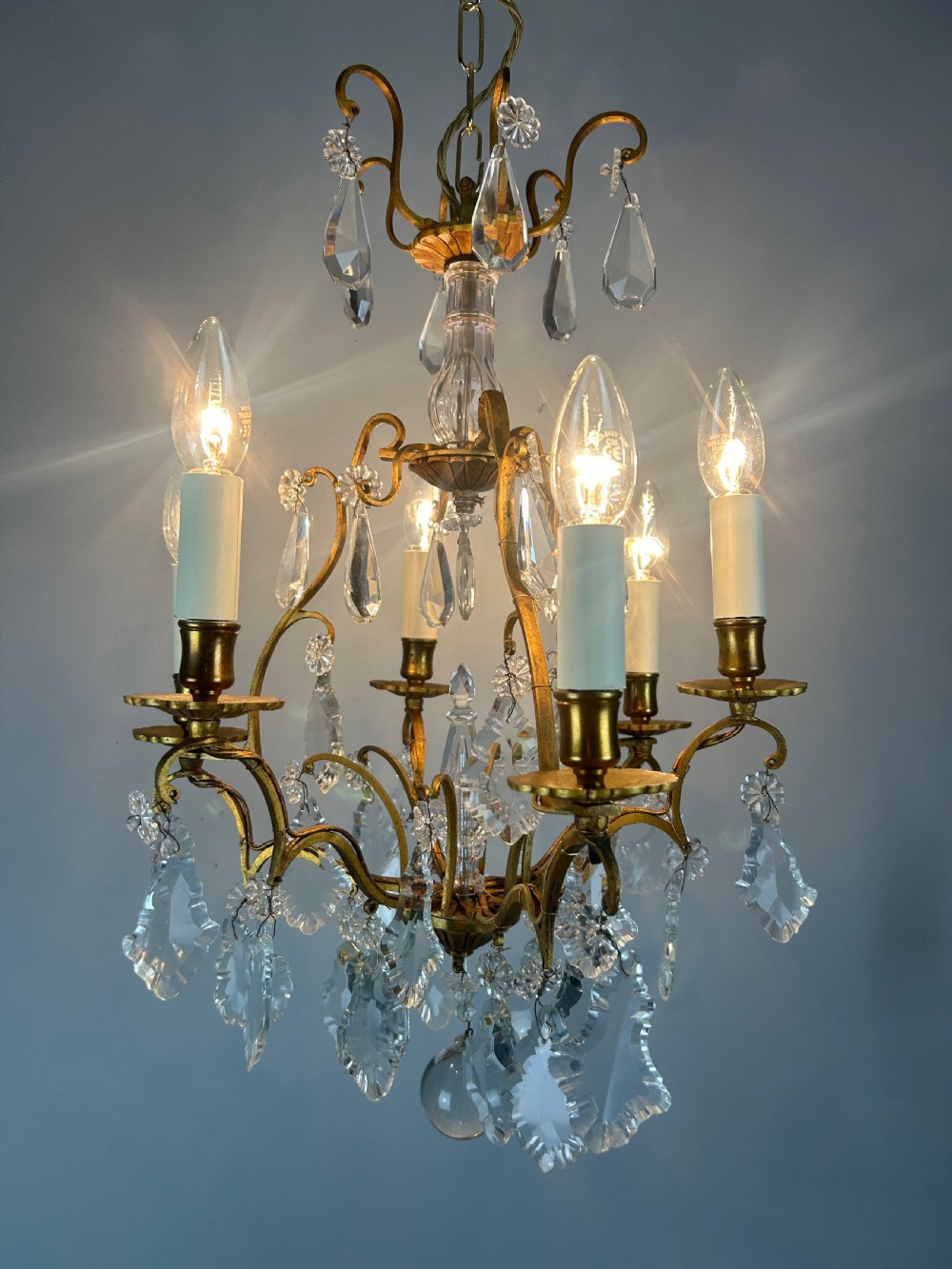 A French brass six-light chandelier featuring curved scroll arms, candle sleeves, and suspended faceted crystal glass droplets. View IX