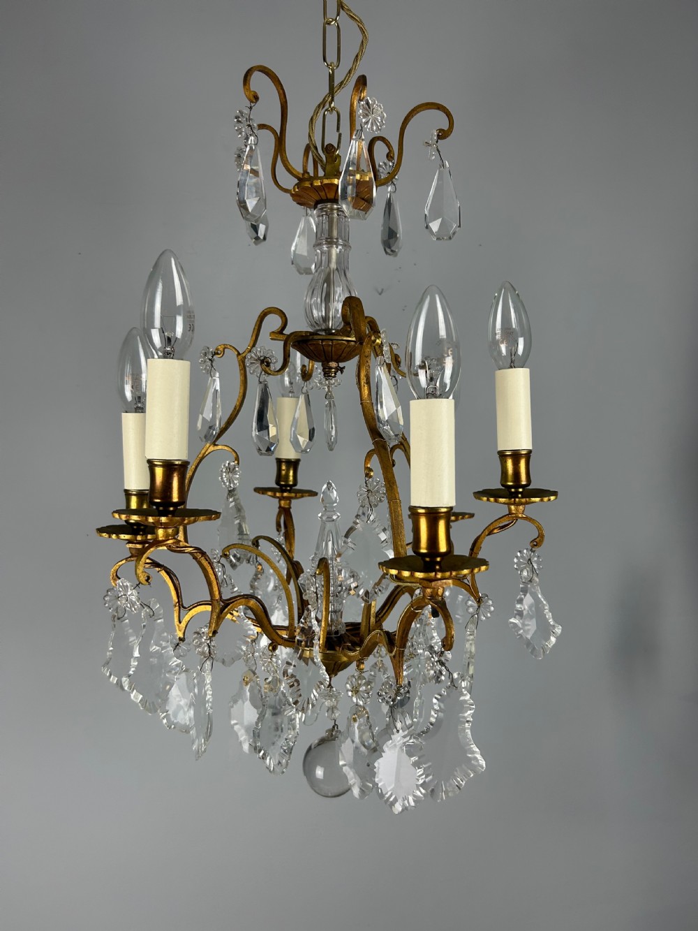 A French brass six-light chandelier featuring curved scroll arms, candle sleeves, and suspended faceted crystal glass droplets. View XII